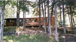 A cabin surrounded by trees, with a stone wall and a wooden deck. - Horsehead Lake Retreat (Big Discounts in June Call 414-378-7273)  (Presque Isle)