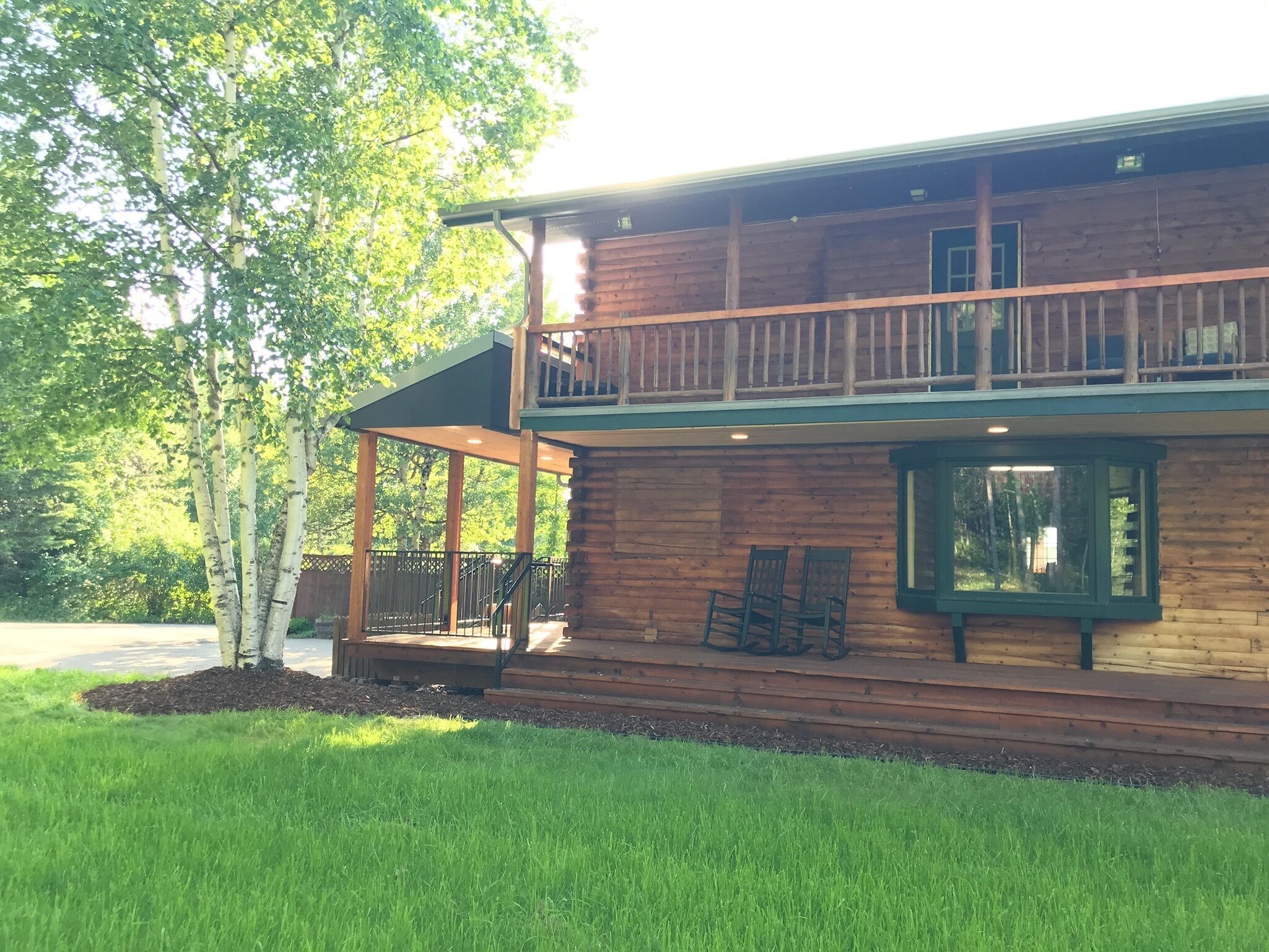 A two-story wooden cabin with a balcony, a covered porch, and a well-maintained lawn.