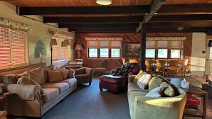 A cozy living room with a wooden ceiling, a sofa, a loveseat, and a dining area with chairs and a table. - Cozy log home sleeps 14 in beds 5.5 baths near Glacier Park and Whitefish Resort (Columbia Falls)