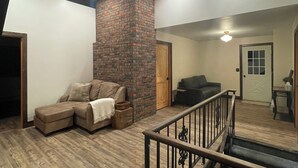 A spacious living area with a wooden ceiling, a brick accent wall, and a ceiling fan. - Cozy log home sleeps 14 in beds 5.5 baths near Glacier Park and Whitefish Resort (Columbia Falls)