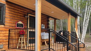 A wooden cabin with a covered porch, a sign indicating it's a Montana homestead, and a grill outside. - Cozy log home sleeps 14 in beds 5.5 baths near Glacier Park and Whitefish Resort (Columbia Falls)