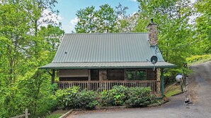 A cabin with a metal roof, a stone chimney, and a porch with a railing.