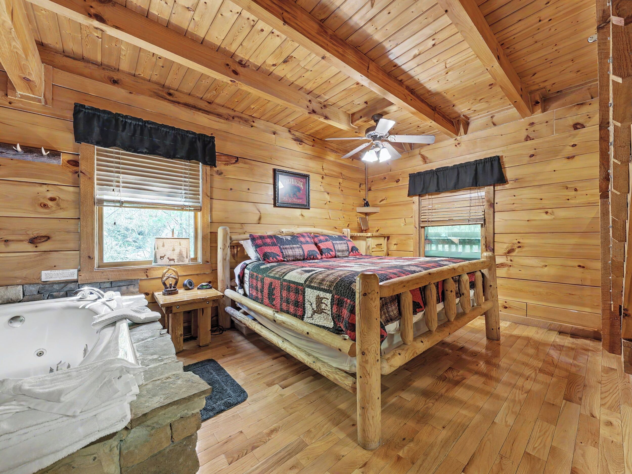 A wooden cabin bedroom with a bed, a nightstand, a ceiling fan, and a window with blinds.