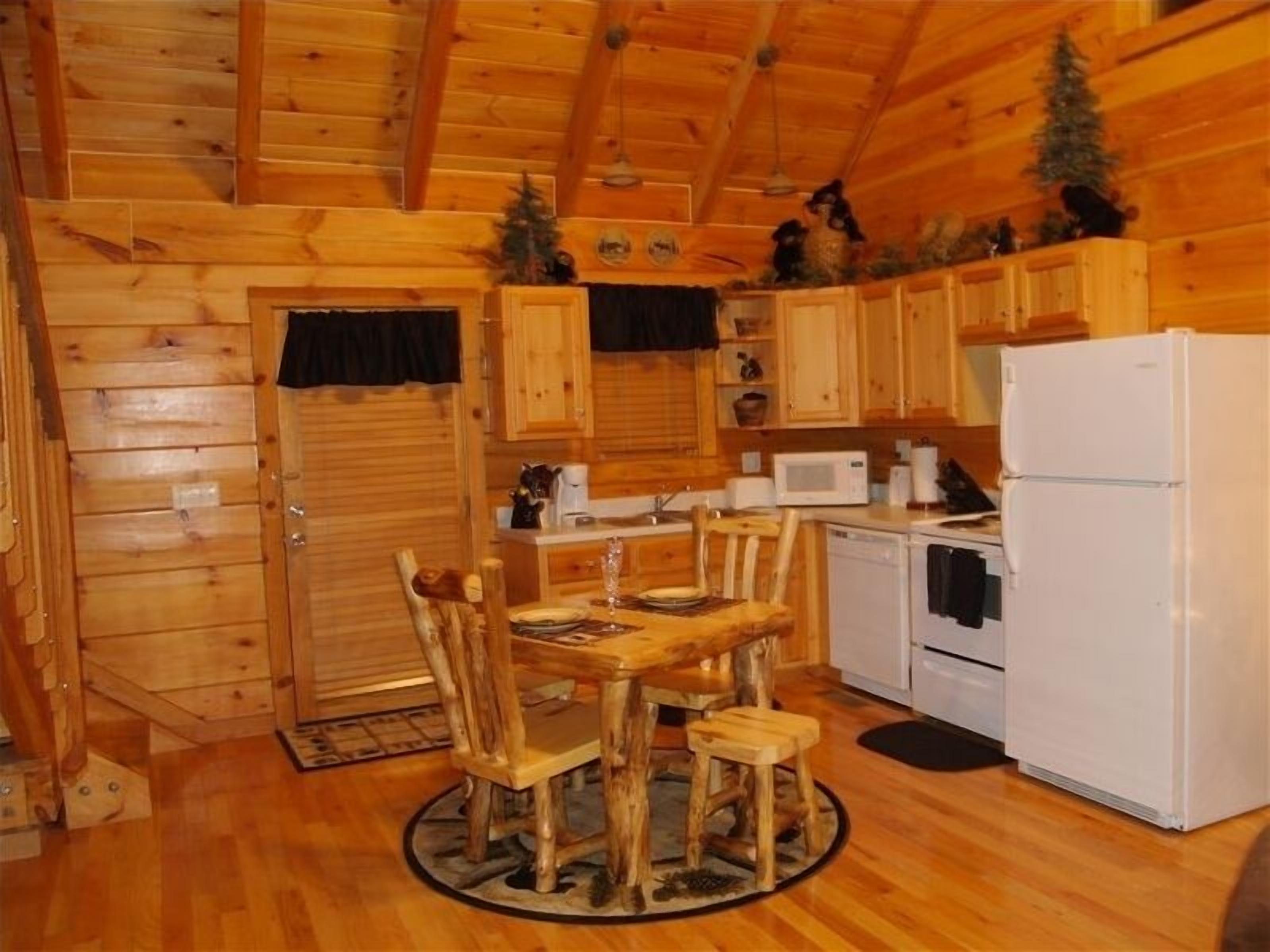 Interno di una baita in legno con un tavolo da pranzo, sedie, un frigorifero, un forno a microonde e un lavello.