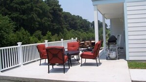 Eine überdachte Terrasse mit Gartenmöbeln, einem Grill und Blick auf einen bewaldeten Hügel.
