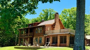 A rustic log cabin with a large porch and multiple windows.
