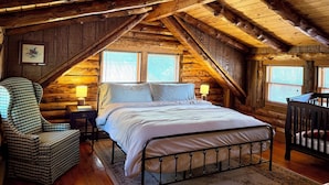 A log cabin bedroom with a loft bed, a chair, and two bedside lamps.