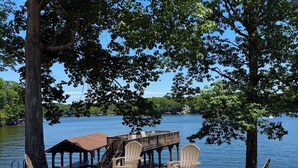 A lakeside deck with Adirondack chairs, a fire pit, and a wooden deck extending over the water.