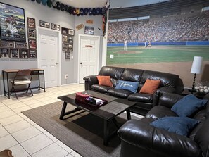 A living room with a black leather couch, a coffee table, and a wall-mounted TV displaying a baseball game. - Downtown Phoenix attached 2 king bed rooms 1 bath suite  (Phoenix)