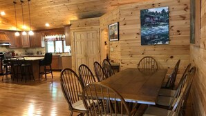 A wooden cabin interior with a dining area, kitchen, and a large window overlooking a river.