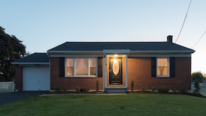 Une maison à deux étages, construite en briques, avec un garage à l’avant, une pelouse bien entretenue et une porte d’entrée éclairée.