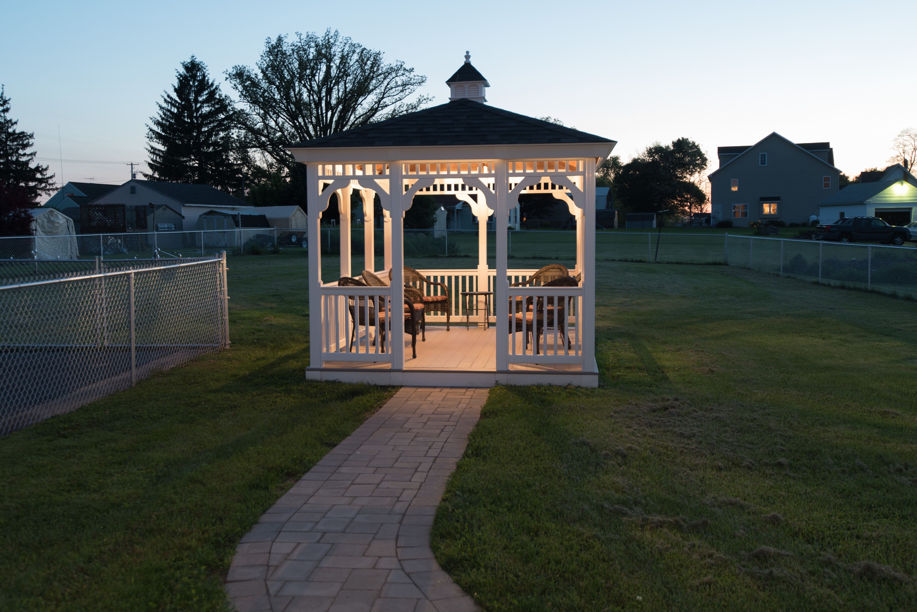 A gazebo with a brick pathway leading to it, surrounded by a chain-link fence.