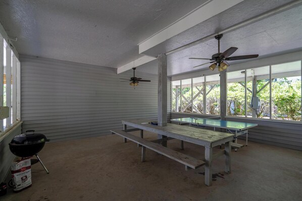 A covered outdoor area with a ping pong table, ceiling fans, and a barbecue grill.