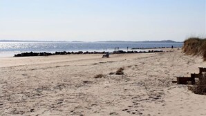 A sandy beach with a clear sky, a few people, and a distant shoreline. - 4 Bedrooms, 4  Baths; Just Steps to the Ocean!  Fronts on Point St. (Edisto Beach)