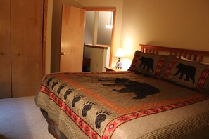 Un dormitorio con una cama que presenta un diseño de oso y huella, un cabecero de madera y una mesita de noche con una lámpara.