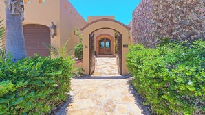 A stone pathway leading to a building with an arched entrance, a garage door, and a stone wall. - Villa #18:  LUXURY 5 Bed/5 bath Oceanfront home for 14 guests.  Renovated 3/26. (Puerto Peñasco)
