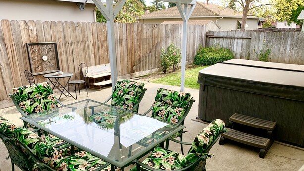 A glass-top patio table with floral chairs, a wooden fence, and a barbecue grill in the background. - Best North Napa Location, Close to Wineries & Restaurants (Napa)