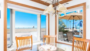Un coin repas avec une table en verre, des chaises en bois et une vue sur la plage.