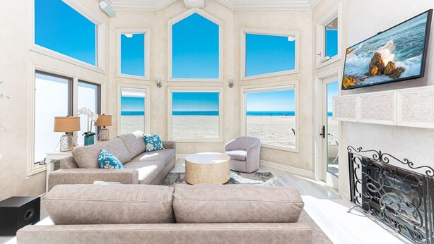 Un salon spacieux doté d’une grande fenêtre donnant sur une plage, d’un coin salon confortable et d’une cheminée.