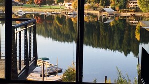 A room with a large window overlooking a calm lake, docked boats, and a forested area. - NOW AVAILABLE FOR LABOR DAY! Coeur d’Alene Luxury Waterfront Condo (Coeur d'Alene)