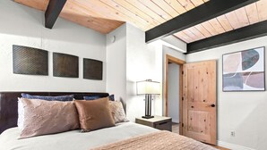 Een slaapkamer met een bed, nachtkastje, lamp, houten deur en drie kunstwerken aan de muur.
