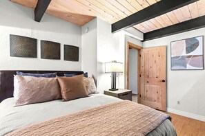 Une chambre à coucher comprenant un lit, une table de chevet, une lampe, une porte en bois et trois œuvres d’art mural.