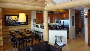 A log cabin interior with a dining area, kitchen, and living room.