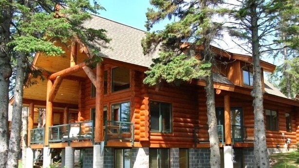A log cabin with a porch, large windows, and a stone foundation.