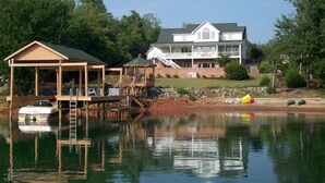 A waterfront property with a large house, a dock, and a covered area with a ladder. - Luxury on Lake Keowee - FALL & Summer 2027 NOW OPEN (Seneca)