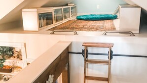 Quarto em estilo loft com teto inclinado, escada de madeira, cama e tapete pequeno.