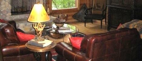 A rustic cabin interior with a stone fireplace, leather sofas, and a chandelier.