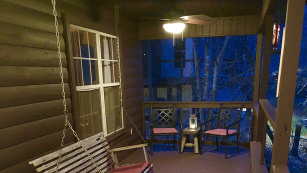 A wooden deck with a swing, a table with chairs, and a lantern.