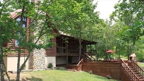 A rustic cabin with a stone foundation, wooden deck, and a covered outdoor seating area.