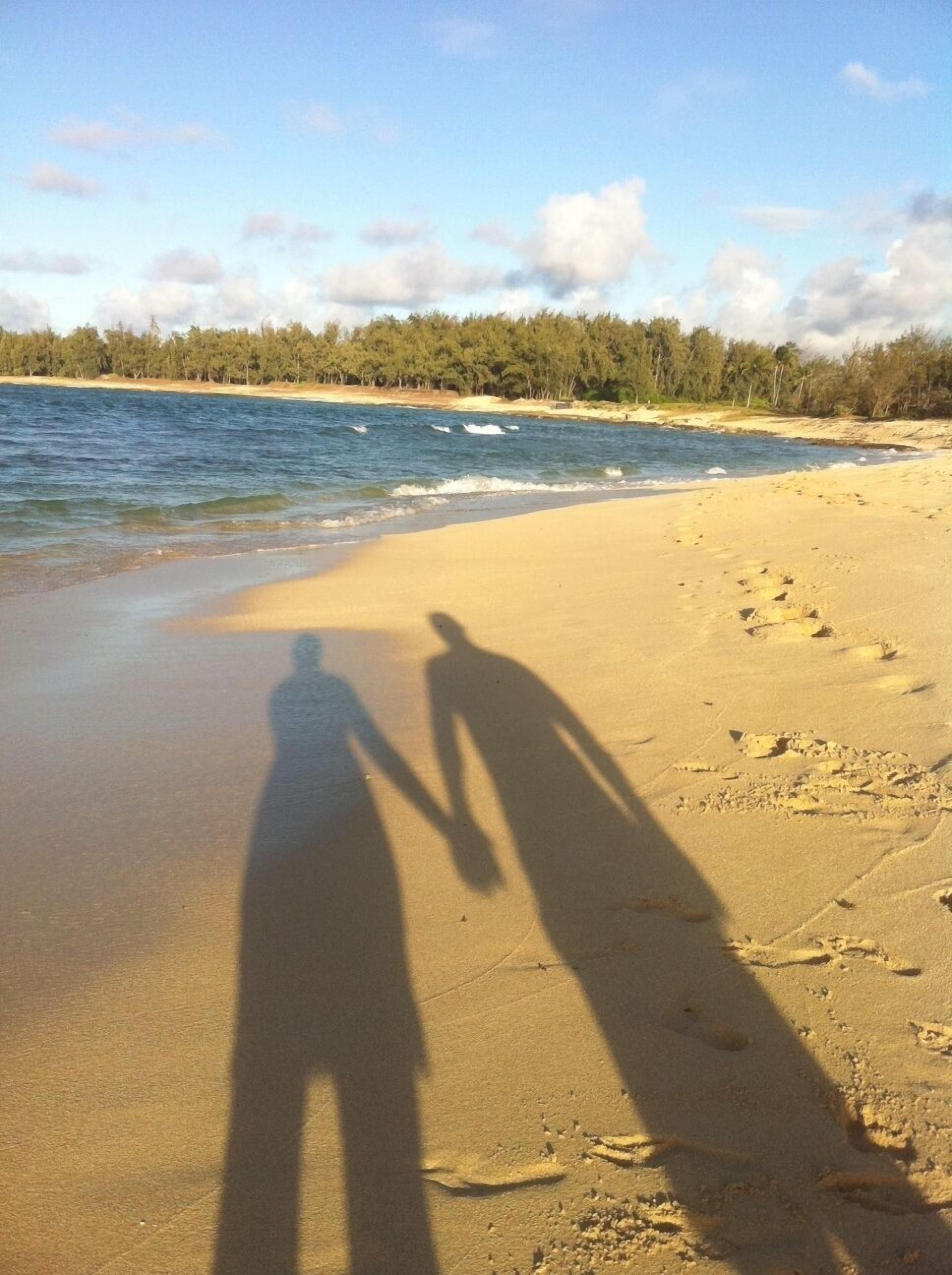 Une plage où l’on peut voir des empreintes de pas et les ombres des personnes sur le sable.