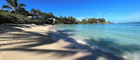 A beach with clear turquoise water, sandy shore, and palm trees.