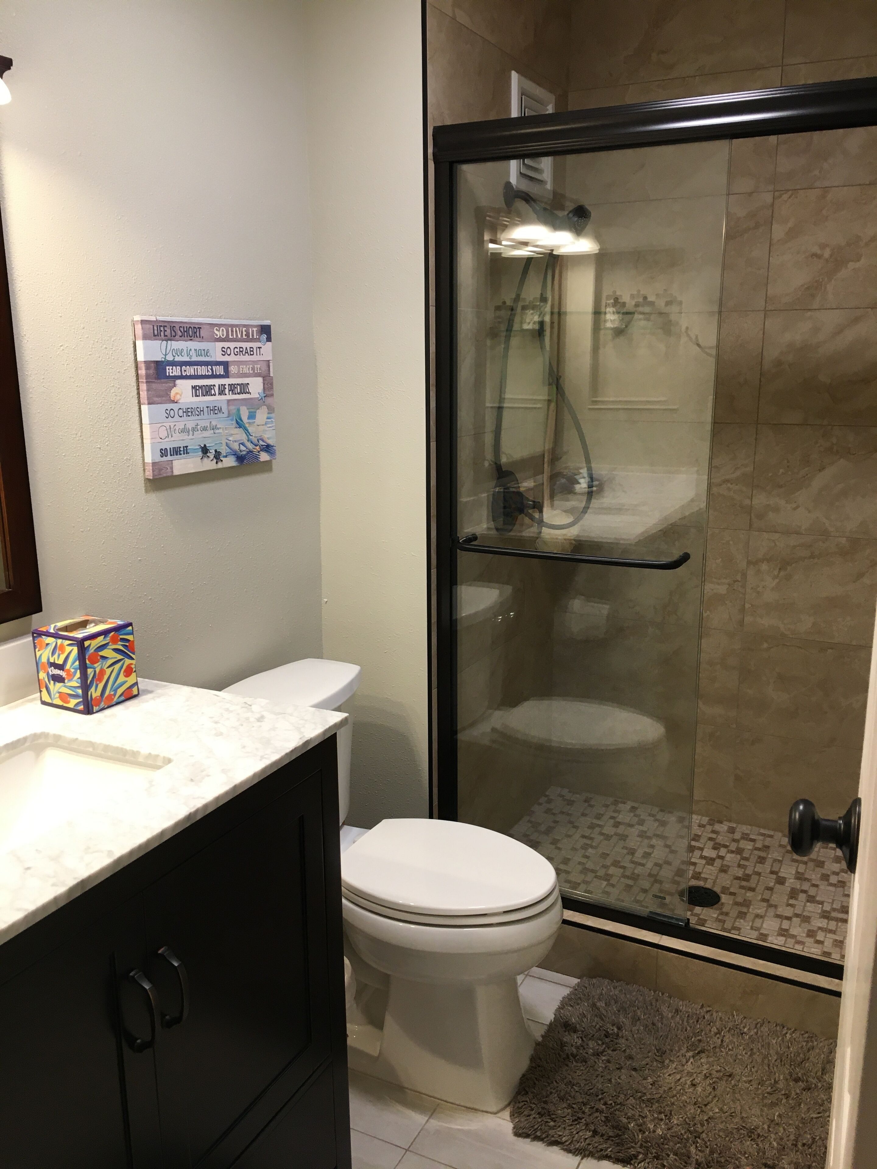 Une salle de bain avec une douche à parois de verre, des toilettes, un meuble-lavabo avec un miroir et une citation inspirante sur le mur.
