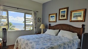 A bedroom with a bed, a window with a view of the sea, and three framed pictures on the wall. - Oceanfront Penthouse Condominium Spectacular Beachfront View (Kihei)
