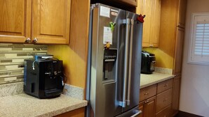 A kitchen with wooden cabinets, a stainless steel refrigerator, a coffee maker, and a built-in oven. - Oceanfront Penthouse Condominium Spectacular Beachfront View (Kihei)