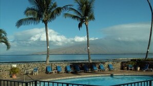A pool area with lounge chairs and palm trees, overlooking a beach and mountains. - Oceanfront Penthouse Condominium Spectacular Beachfront View (Kihei)