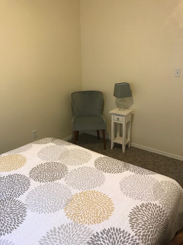 A bedroom with a bed, a chair, and a nightstand with a lamp.