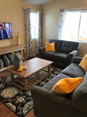 A living room with a grey sofa, a wooden coffee table, and patterned curtains.