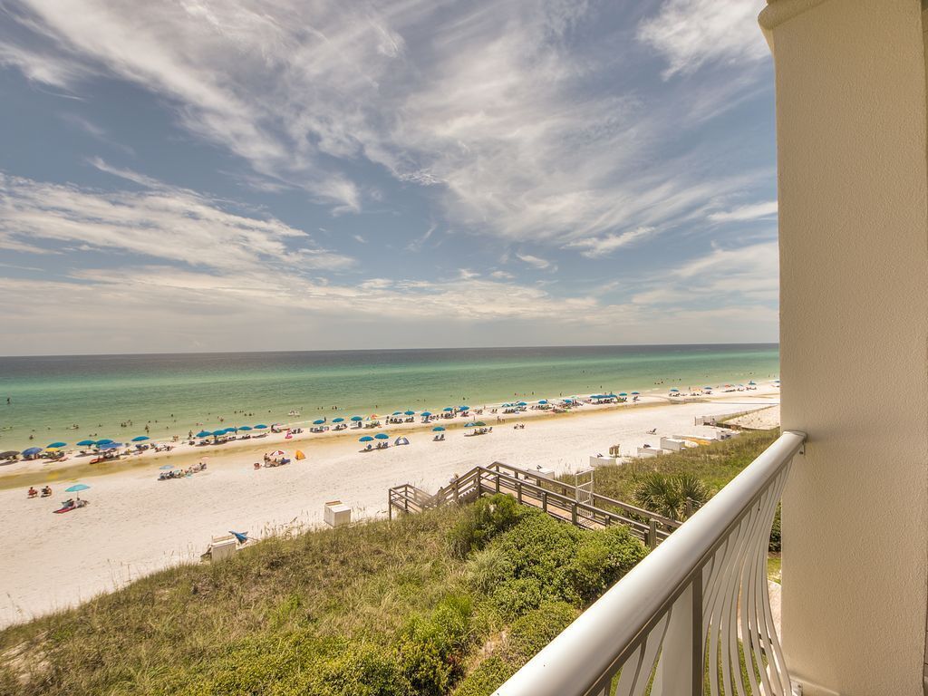 A beach view from a balcony with a clear sky, sandy beach, and umbrellas.
