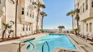 A pool area with a clear blue pool, surrounded by lounge chairs and palm trees, with a view of the ocean in the background. - GULF-FRONT, Cancellation, Balcony, Grill, Pool, Updated! (Santa Rosa Beach)