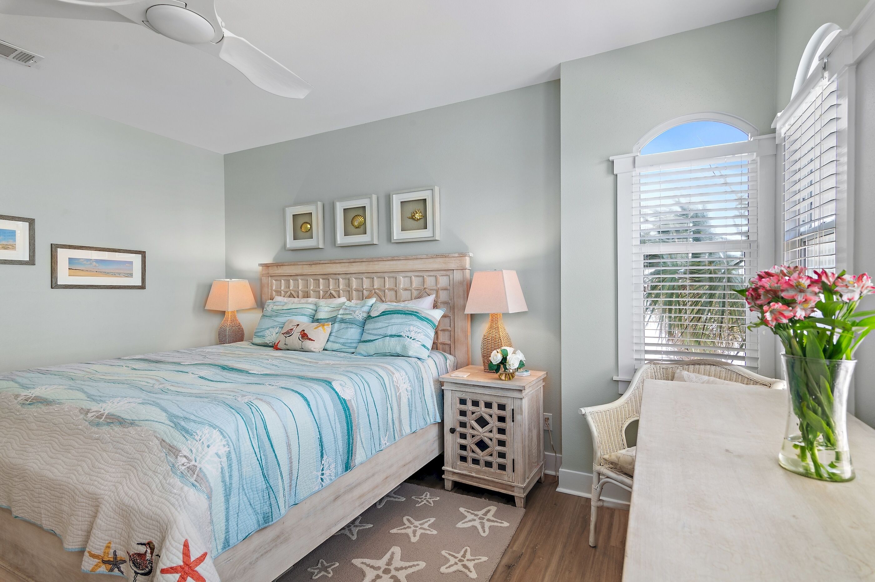 A bedroom with a bed, bedside tables, a chair, a window with blinds, and wall-mounted pictures.