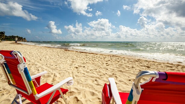 A beach with red beach chairs and a clear sky.