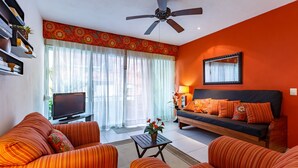 A living room with orange walls, a ceiling fan, a sofa, a coffee table, and a TV.