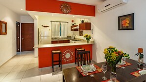 A compact kitchen with a central island, a dining area with a table set for two, and a wall-mounted air conditioner.