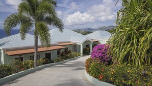 Un chemin menant à un bâtiment doté d’un toit incurvé, entouré de plantes et de fleurs tropicales.