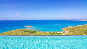 Une piscine à débordement offrant une vue imprenable sur l’océan et une petite île.