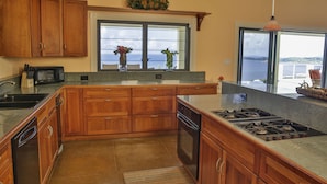 Une cuisine avec des meubles de rangement en bois, une cuisinière encastrée et une fenêtre donnant sur la mer.